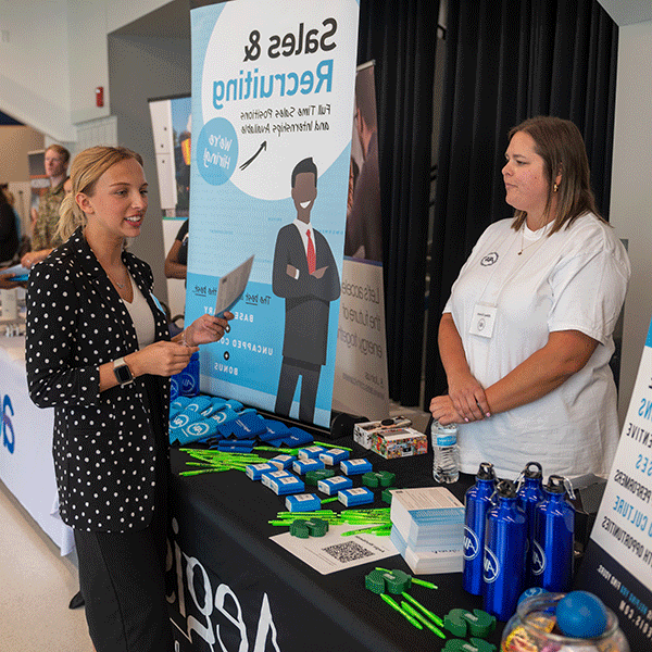 A photo of two women talking with one another at a job fair.