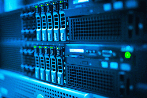 Cold blue light shines on the backside of a computer terminal, illuminating the ports, switches, HDMI inputs, vents, and other components of the machine. Some green lights are illuminated.