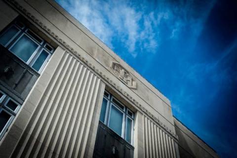 AN ANGLED IMAGE TAKEN UPWARD OF AN ORNATE GOVERNMENT BUILDING WITH A FLAT ROOF AND BLUE SKY